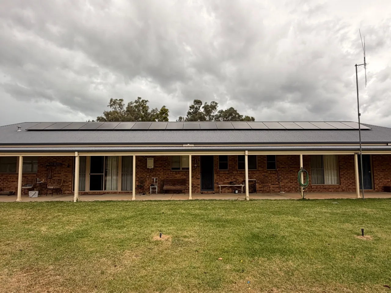 Long row of black solar panels across the roof of a single-storey brick home with a wide verandah