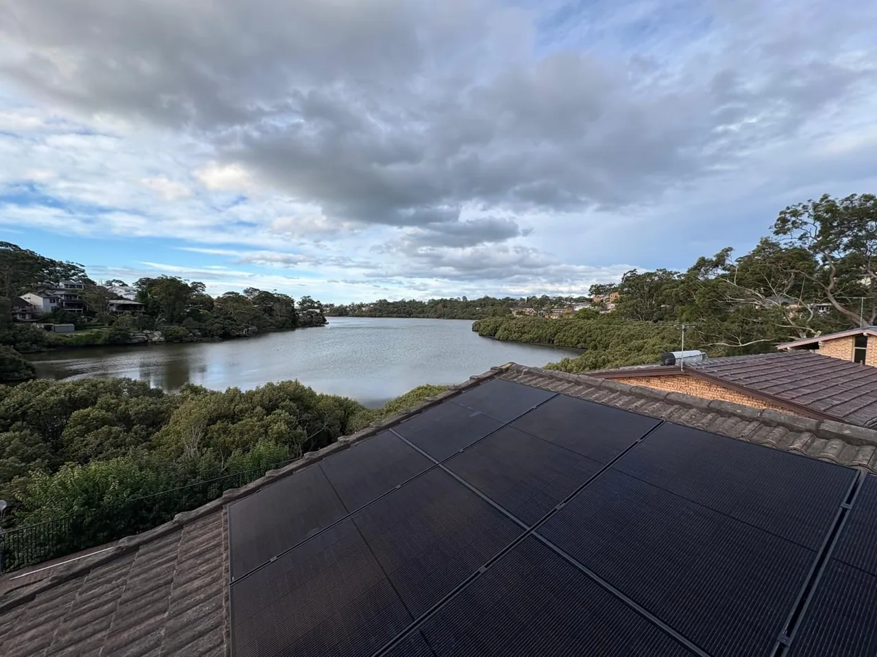 Rooftop solar array looking out over a river and tree-lined suburban homes