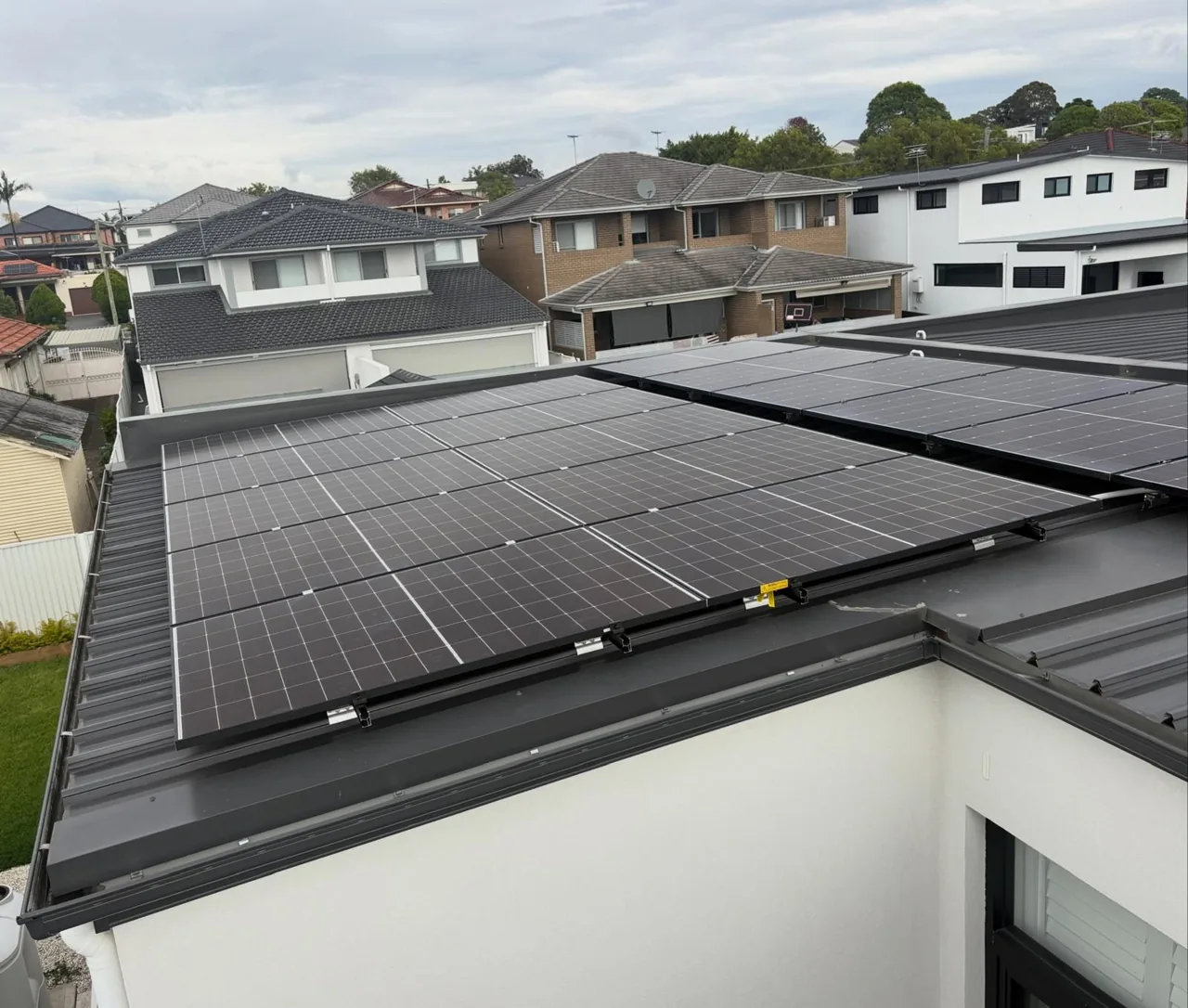 Commercial-style solar array covering a flat metal roof above neighbouring houses