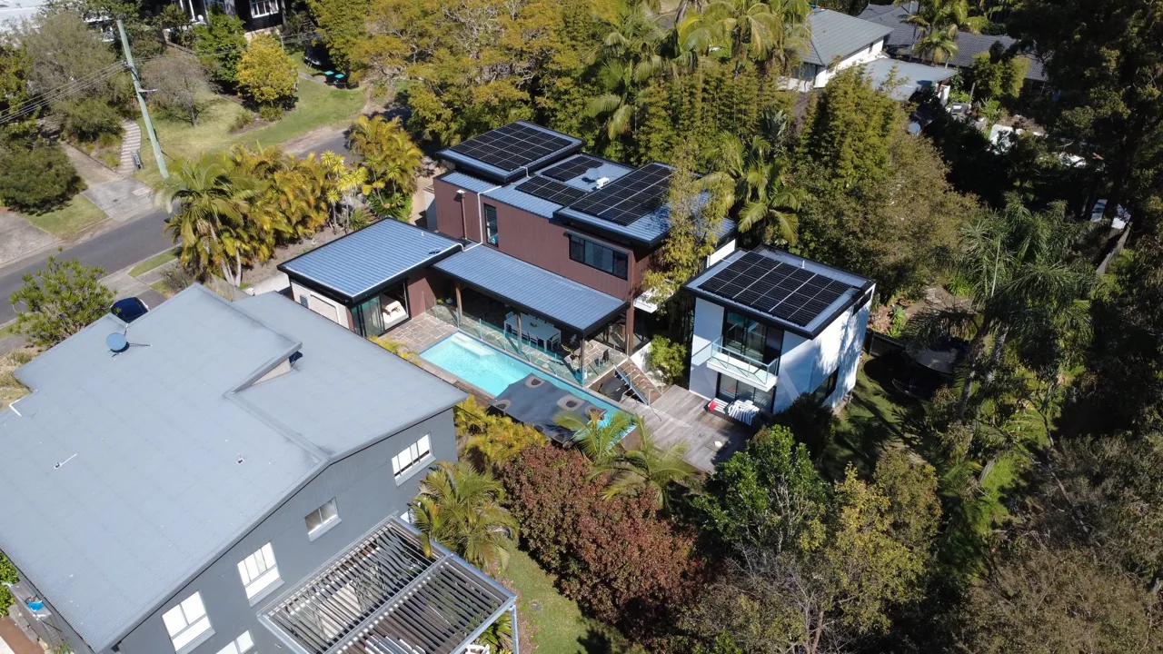 Black solar panels across the roof of a modern home beside a backyard swimming pool