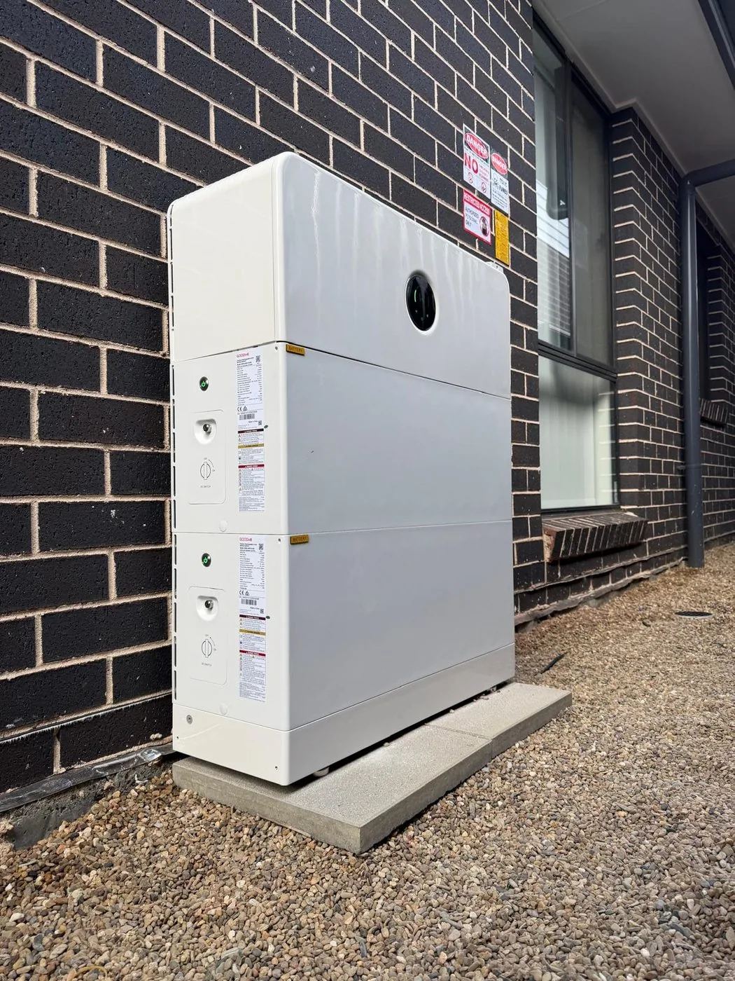 White GoodWe ESA modular battery mounted against a dark brick exterior wall