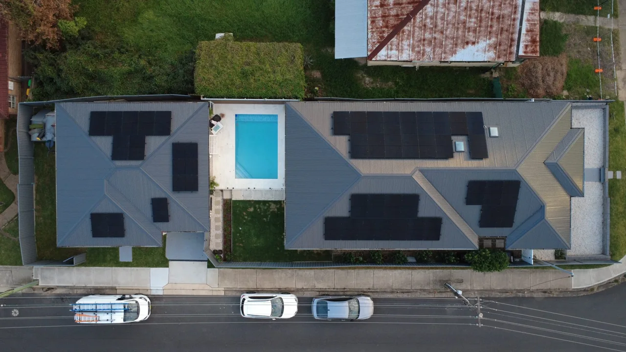 Top-down drone shot of solar arrays along a long duplex roof next to a pool
